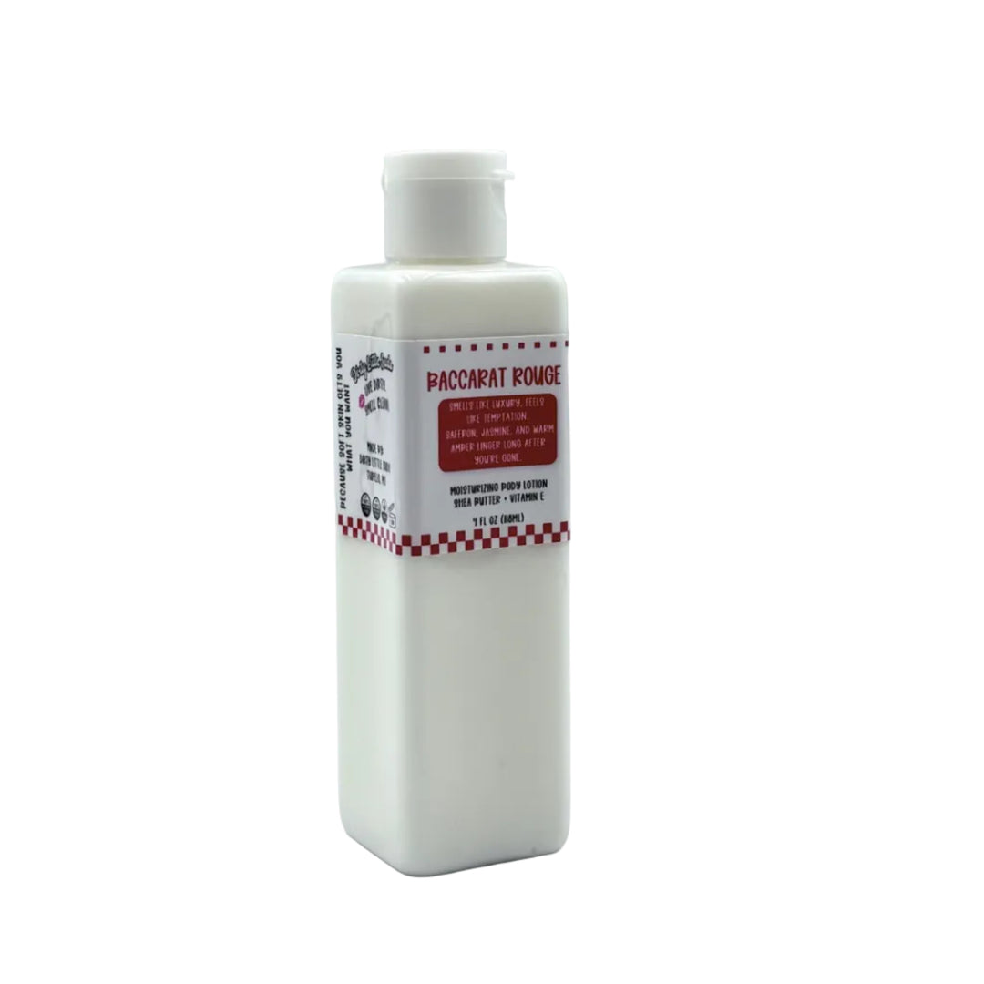 Dirty Little Suds Baccarat Rouge body lotion in a white rectangular bottle with flip-top cap and red label, featuring a warm amber, saffron, and jasmine scent.