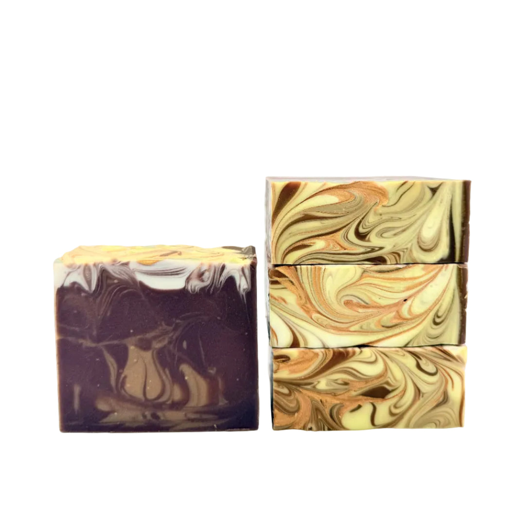Three rectangular artisan soap bars with marbled swirls, displayed on a white reflective surface. One bar stands upright on the left, while two stacked bars stand on the right.