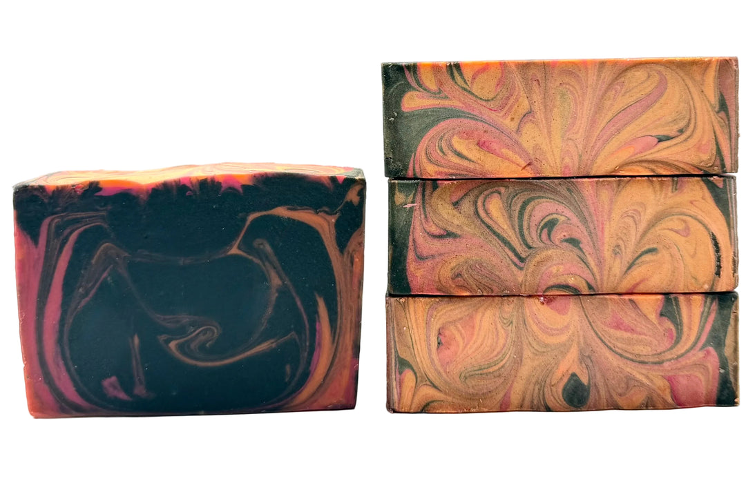 Handmade soap bars with dark charcoal base and swirling amber, gold, and rose tones in a marbled pattern