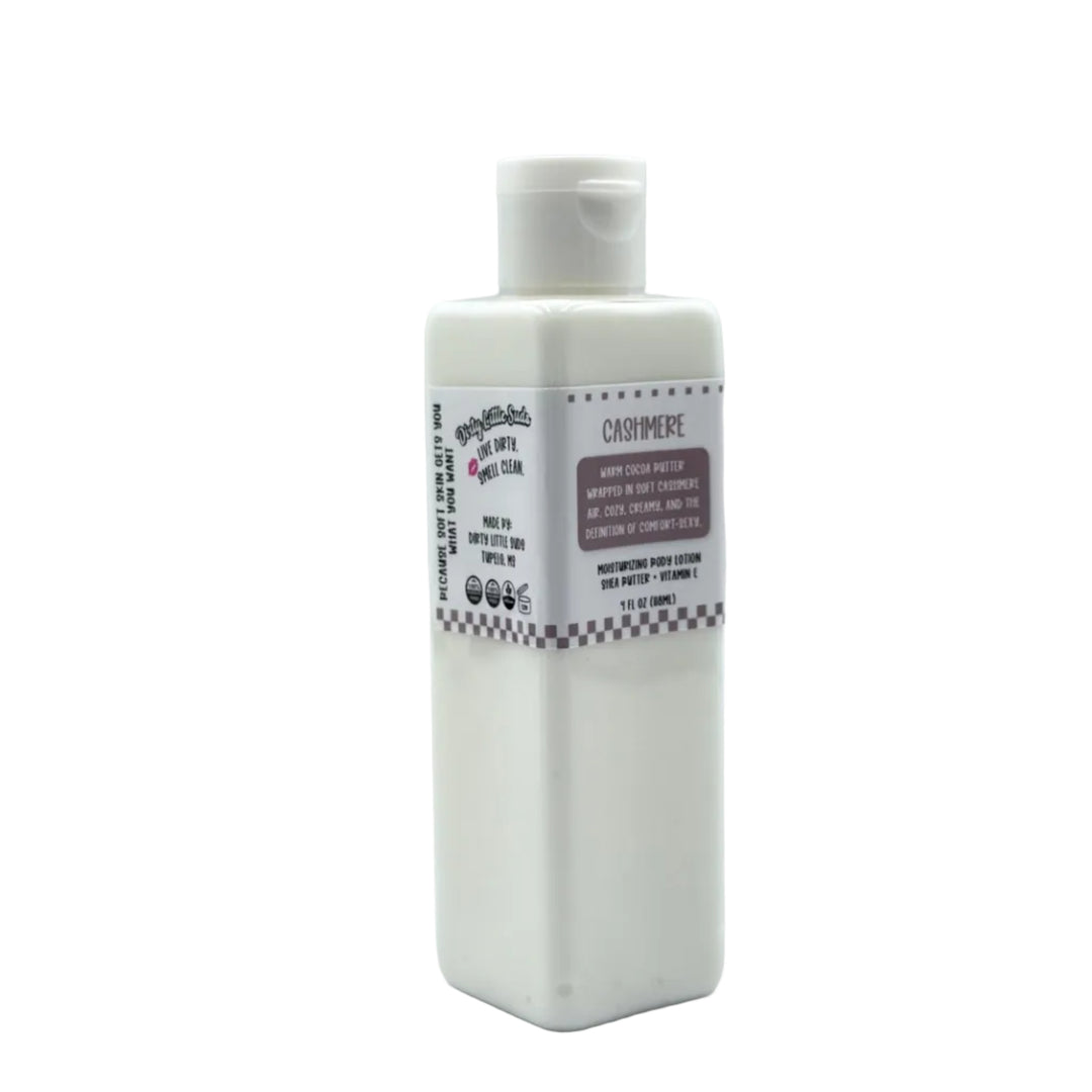 Dirty Little Suds Cashmere body lotion in a white rectangular bottle with flip-top cap and taupe label, featuring a warm cocoa butter, vanilla, and soft cashmere scent.