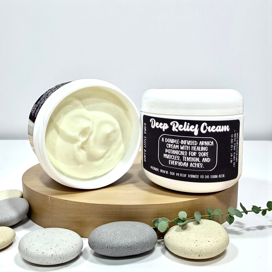 Open jar of Dirty Little Suds Deep Relief Cream showing creamy texture next to sealed jar and spa stones.