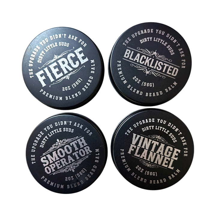Four black matte tins of Dirty Little Suds Beard Balm from the Rough Cut Collection, premium men’s grooming lineup in multiple scents for conditioning, shaping, and softening beards.
