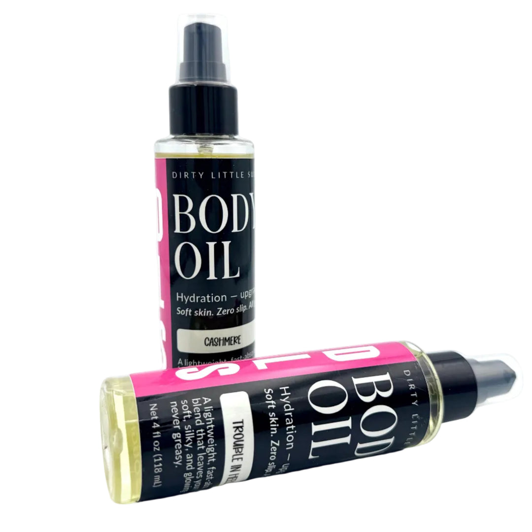 Two 4 oz Dirty Little Suds Body Oil bottles featuring the new label design in Cashmere and Trouble in Heels scents on a white background. Lightweight, fast-absorbing body oil that leaves skin soft, radiant, and never greasy.
