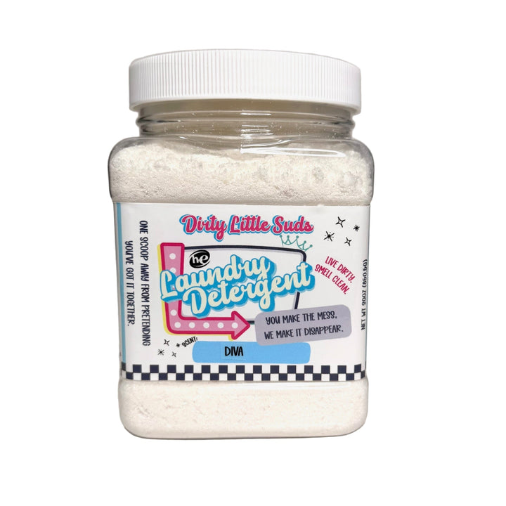 Clear square jar of Dirty Little Suds HE Laundry Detergent in the Diva scent. White powdered detergent with a retro pin-up inspired label in pink, turquoise, and black. Tagline reads “You make the mess. We make it disappear.” A glamorous, bold laundry fragrance for those who want their clothes to smell unforgettable.