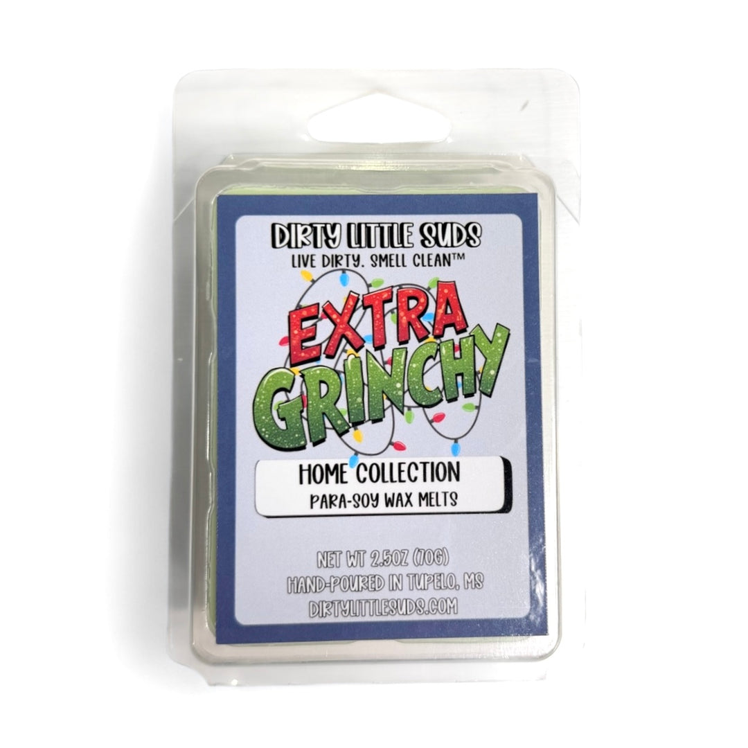 Clamshell pack of Dirty Little Suds Extra Grinchy wax melt with a retro-inspired label. A festive holiday fragrance of red apples, berries, orange, and cinnamon wrapped in amber and musk for a cozy, mischievous Christmas scent.
