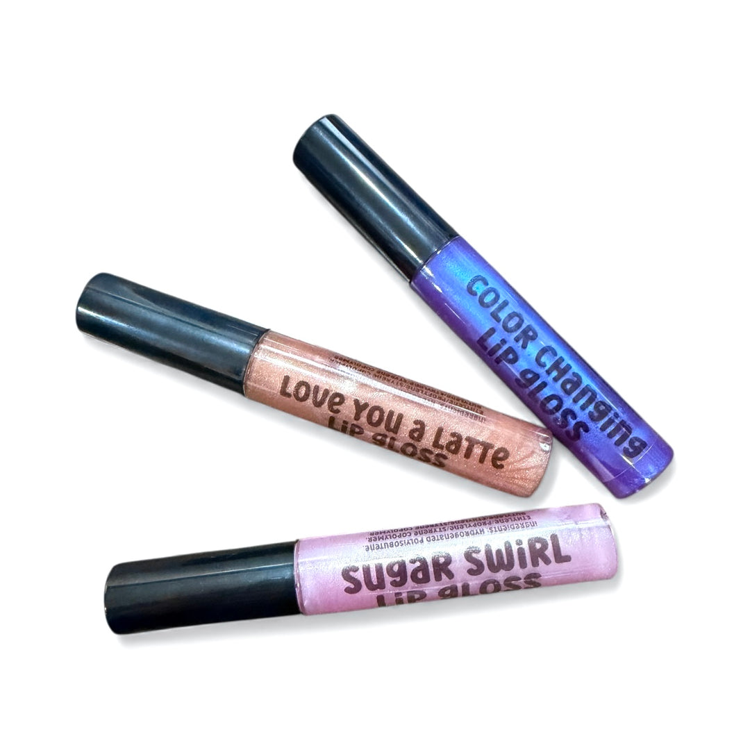 Three Dirty Little Suds lip gloss tubes arranged diagonally, featuring Sugar Swirl (pink), Love You a Latte (nude shimmer), and the Color-Changing gloss (purple) | Dirty Little Suds