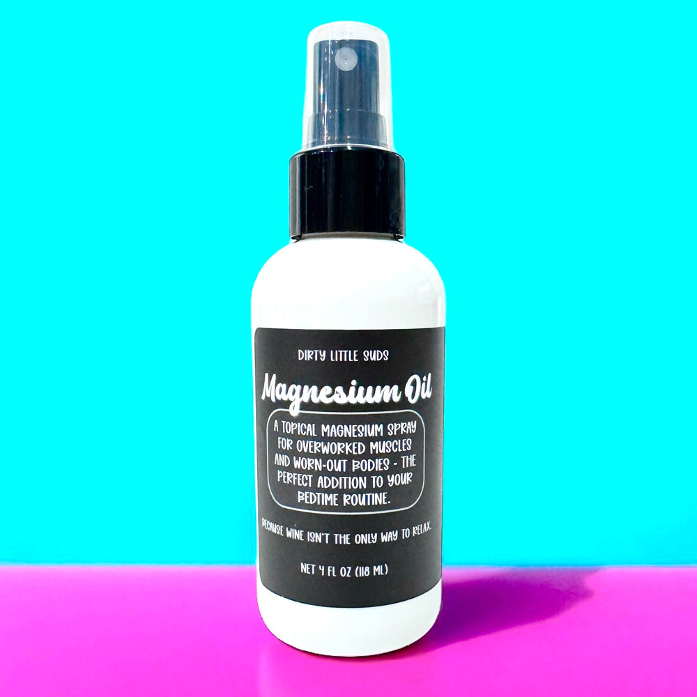 White 4oz spray bottle of Dirty Little Suds Magnesium Oil with a black label, displayed against a bright turquoise and hot pink background. The label reads “A topical magnesium spray that helps relax muscles, ease tension, and support restful sleep—because your body deserves a break