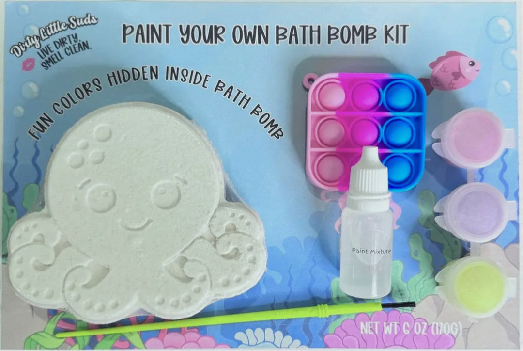Dirty Little Suds Paint Your Own Bath Bomb Kit featuring an octopus bath bomb, colorful paint pots, brush, mixing dropper, and rainbow pop-it fidget toy on ocean-themed packaging.