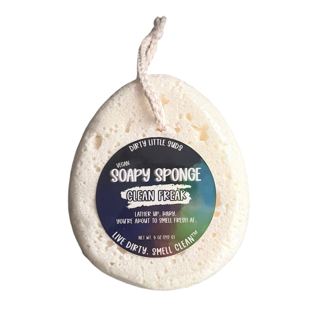 Dirty Little Suds Soapy Sponge in Clean Freak scent – white vegan sponge with holographic label and hanging string, featuring bright notes of apple, mango, peach blossom, and musk; sulfate, paraben, and phthalate free.