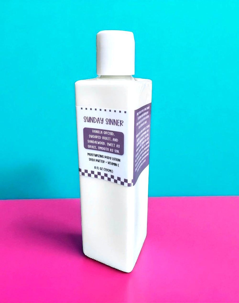 White rectangular 8oz bottle of Dirty Little Suds Sunday Sinner Body Lotion with a deep purple retro label featuring checkerboard accents. The label highlights notes of vanilla orchid, sugared violet, and sandalwood, described as “sweet as grace, smooth as sin.” Displayed against a turquoise and hot pink background for a bold vintage pin-up aesthetic.