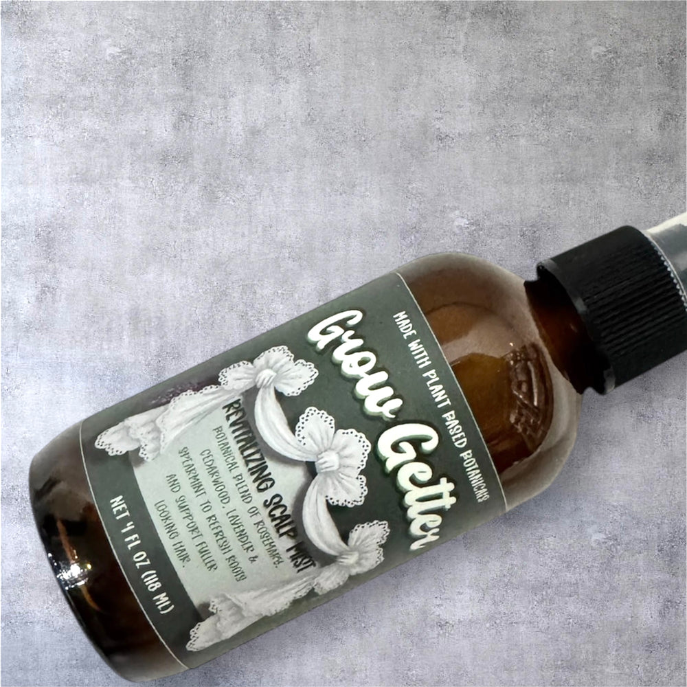 Amber spray bottle of Grow Getter Revitalizing Scalp Mist lying on gray textured background, showcasing vintage-inspired Dirty Little Suds label.