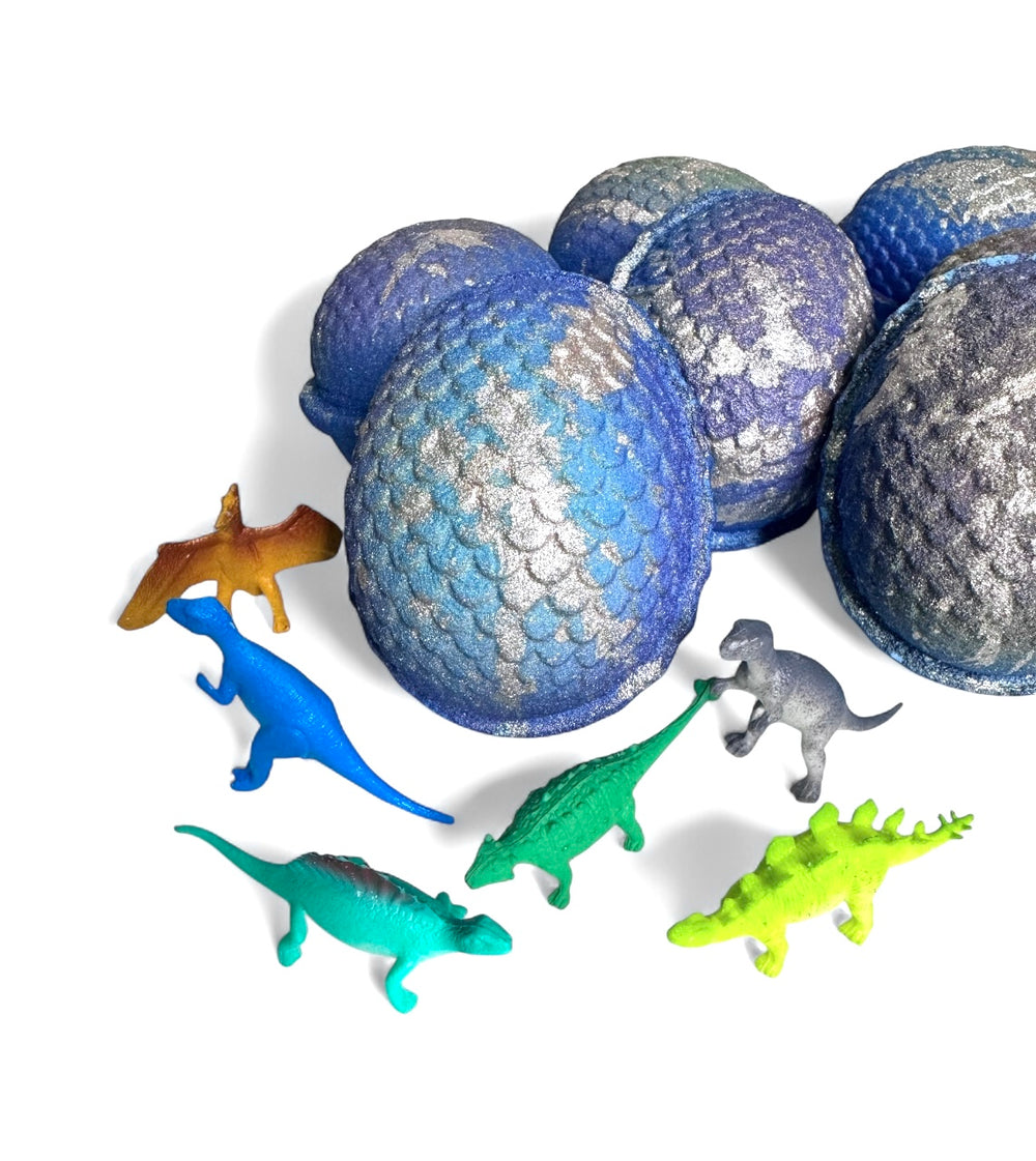 Several glittery blue and silver dino egg bath bombs surrounded by colorful plastic dinosaur toys revealed inside each bomb.