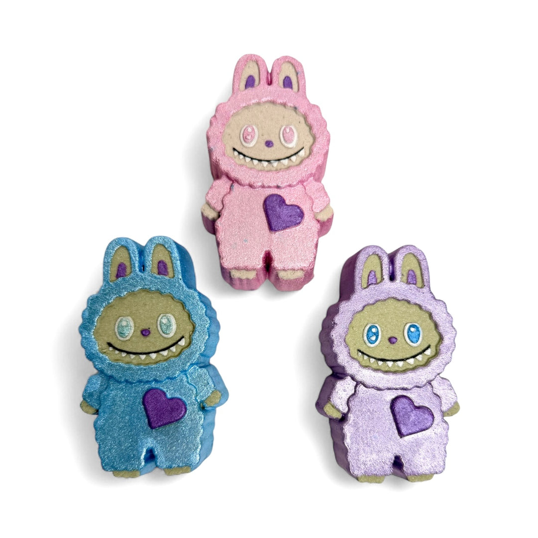 Three hand-painted Labubu Full Body Bath Bombs in pink, blue, and purple with heart details. Each 6oz bath bomb is scented in Smell the Rainbow and filled with colorful embeds for rainbow fizz and foam.
