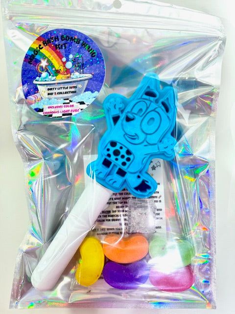 Holographic gift bag containing the Magic Bath Bomb Wand Kit by Dirty Little Suds. Features a blue dog bath wand, colorful jelly bean bath bombs, a flashing light cube, and holographic sticker.