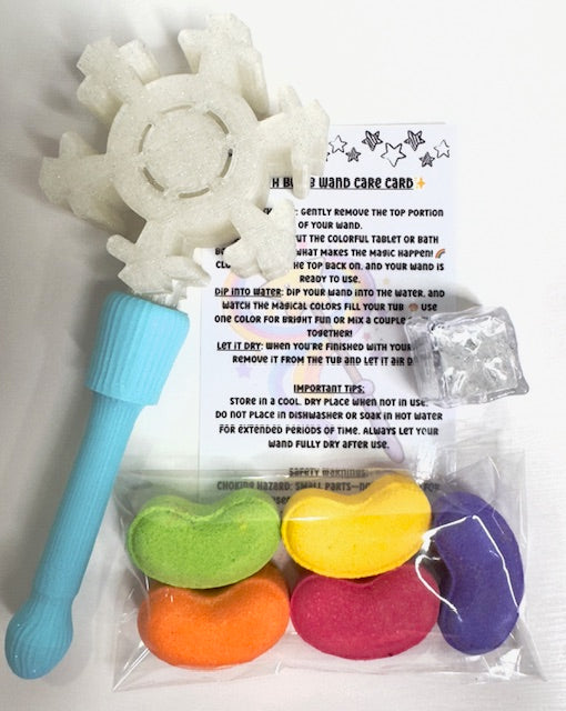 Snowflake bath wand kit contents displayed on white background. Includes white snowflake wand with blue handle, rainbow jelly bean bath bombs, flashing cube, and printed care card.