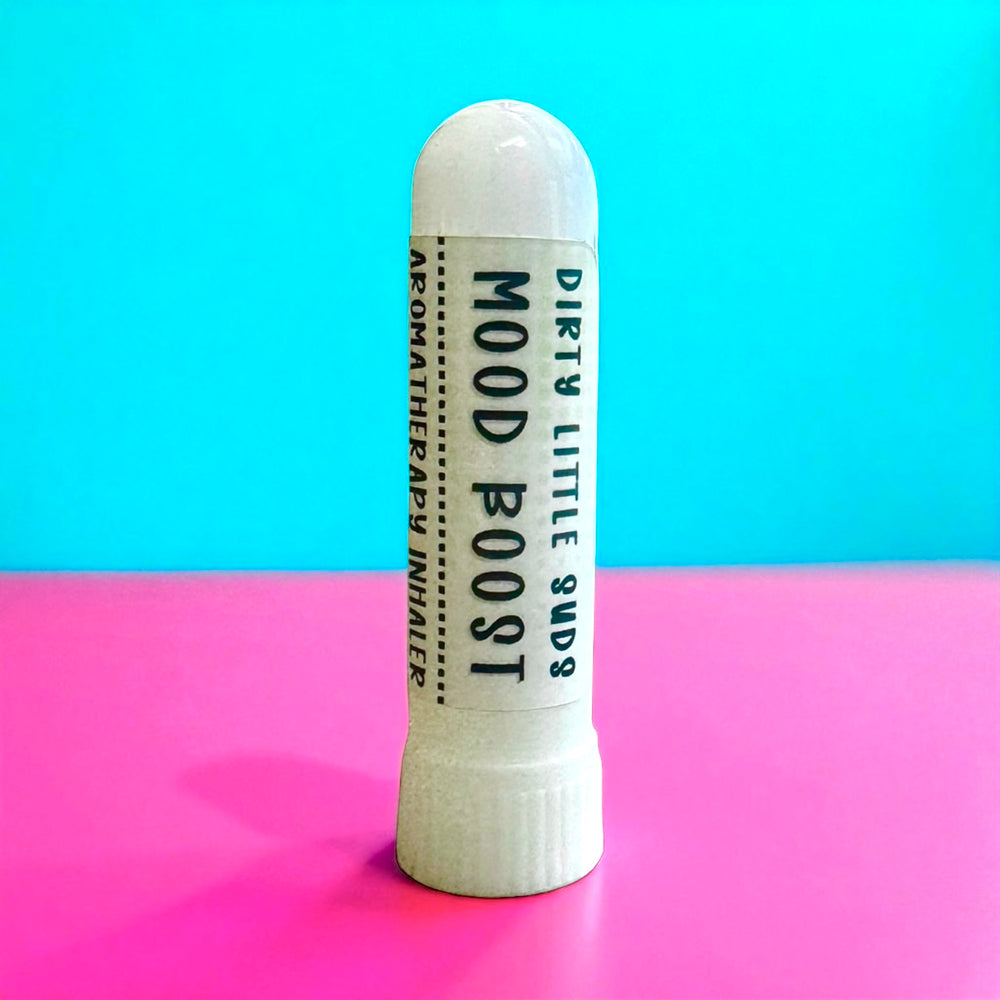 Dirty Little Suds Mood Boost Aromatherapy Inhaler on bright pink and turquoise retro background, portable essential oil stick made with orange, grapefruit, lavender, spearmint, and cedarwood for stress relief and uplift.