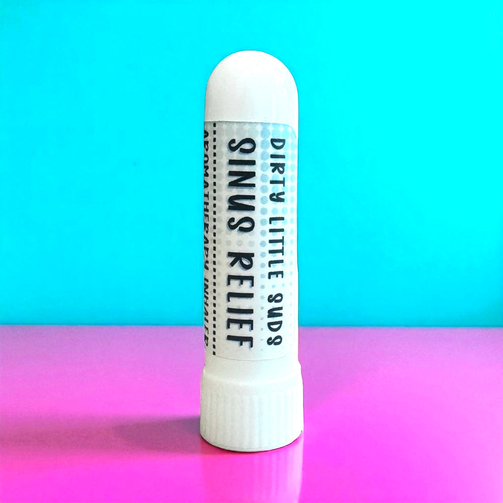 Dirty Little Suds Sinus Relief Aromatherapy Inhaler on bright pink and turquoise retro background, portable essential oil stick with peppermint, eucalyptus, rosemary, and spearmint for natural congestion relief.
