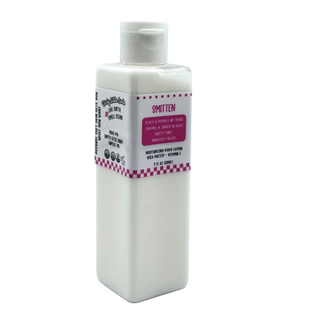 Dirty Little Suds Smitten body lotion in a white rectangular bottle with flip-top cap and pink label, featuring a sweet peach, berry, caramel, and ginger scent.