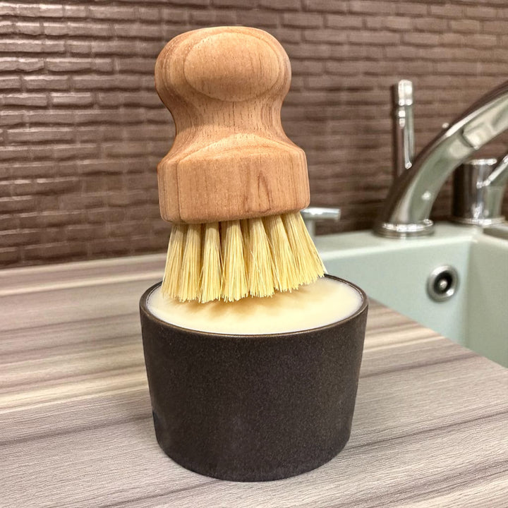 Wooden scrub brush resting on solid dish soap ramekin by sink – sustainable, plastic free kitchen cleaner with natural lemon scent