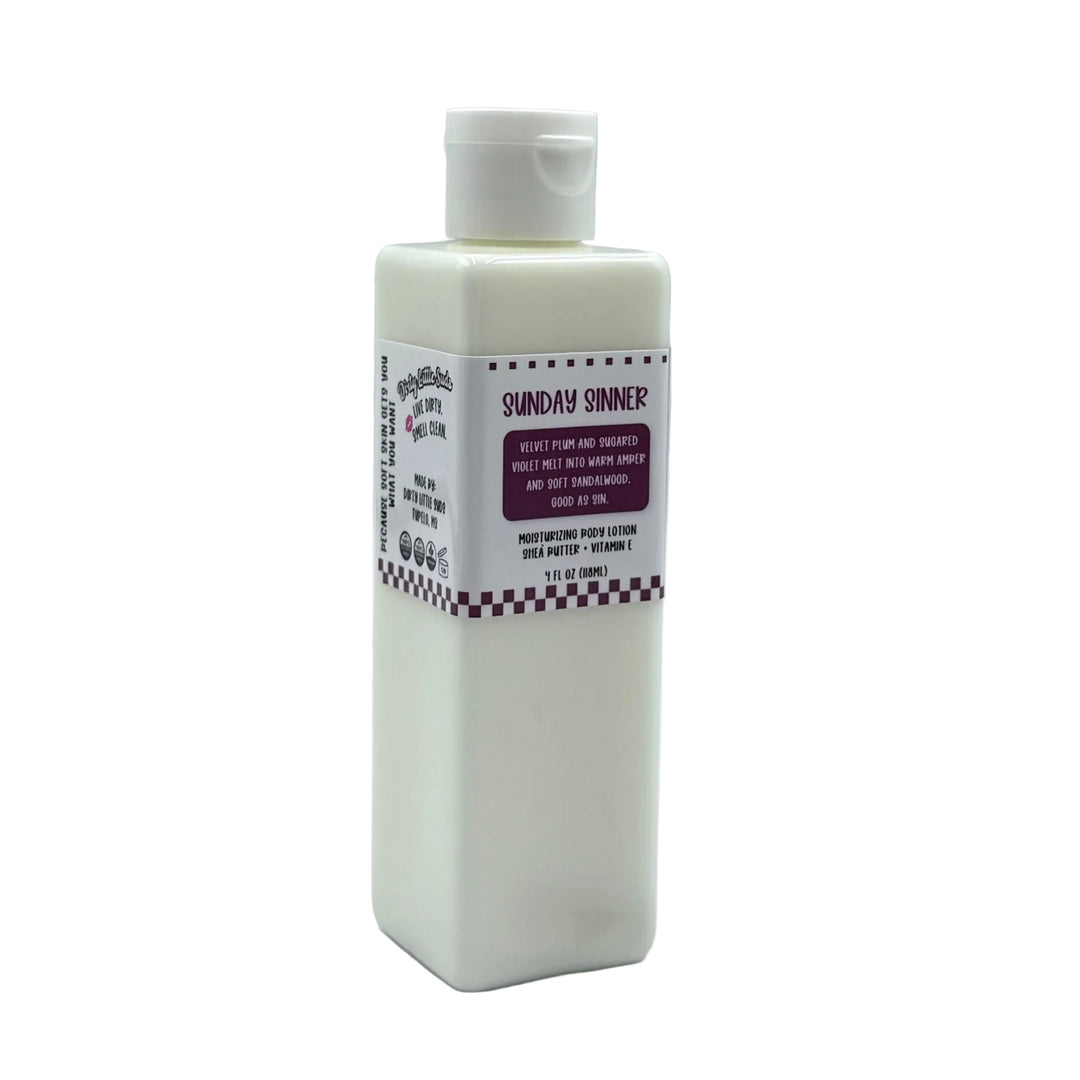 Dirty Little Suds Sunday Sinner body lotion in a white rectangular bottle with flip-top cap and deep plum label, featuring a warm plum, violet, amber, and sandalwood scent.