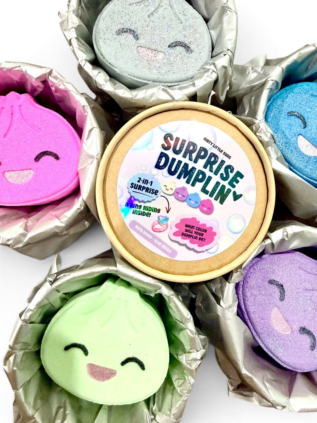 Colorful Surprise Dumplin bath bombs surrounding a packaged mystery bath bomb with a hidden costume jewelry ring inside.