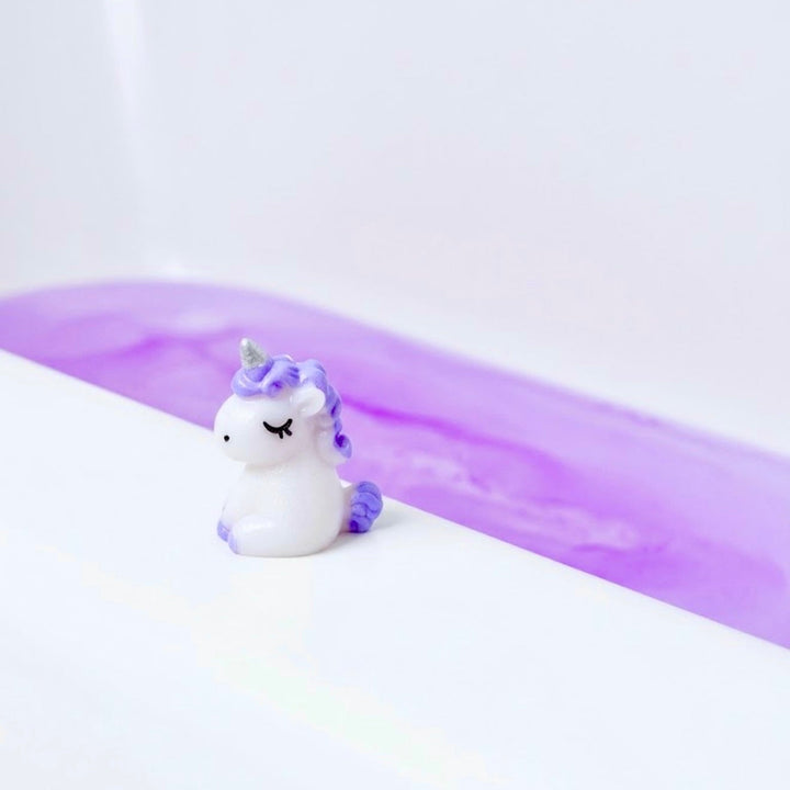 Tiny surprise unicorn toy revealed from a Unicorn Horn Bath Bomb beside purple bath water