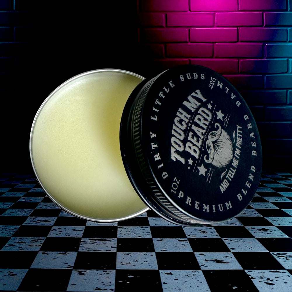 Open tin of Touch My Beard Premium Blend Beard Balm from Dirty Little Suds, displayed on a checkered surface with neon brick wall background.