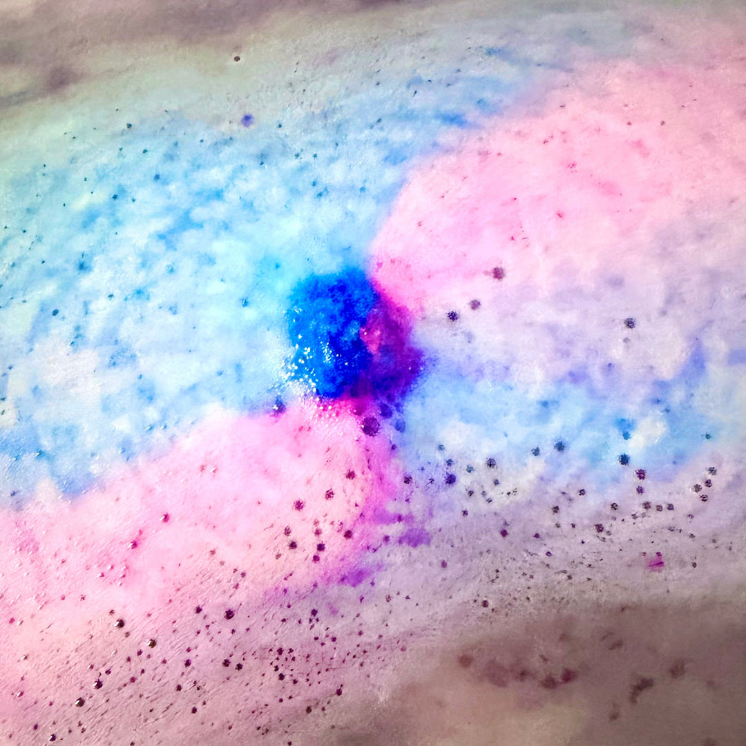 Vibrant swirl of pink, purple, and blue fizz from a Unicorn Tub Tab dissolving in water.